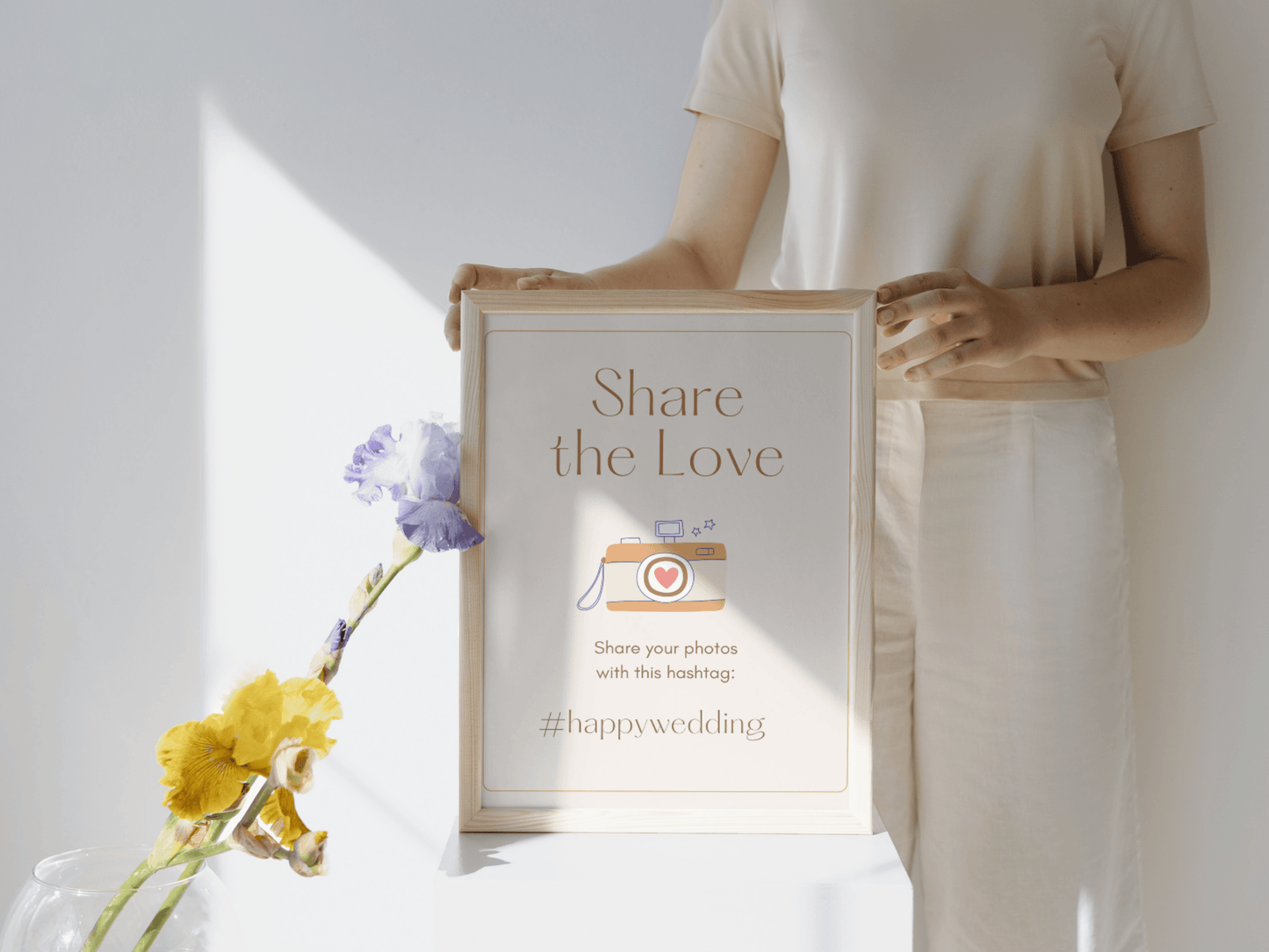 Woman holding a boho and aesthetic wedding sign template which says: "Share the Love; share tour photos with this hashtag: #happywedding". It's editable in Canva.